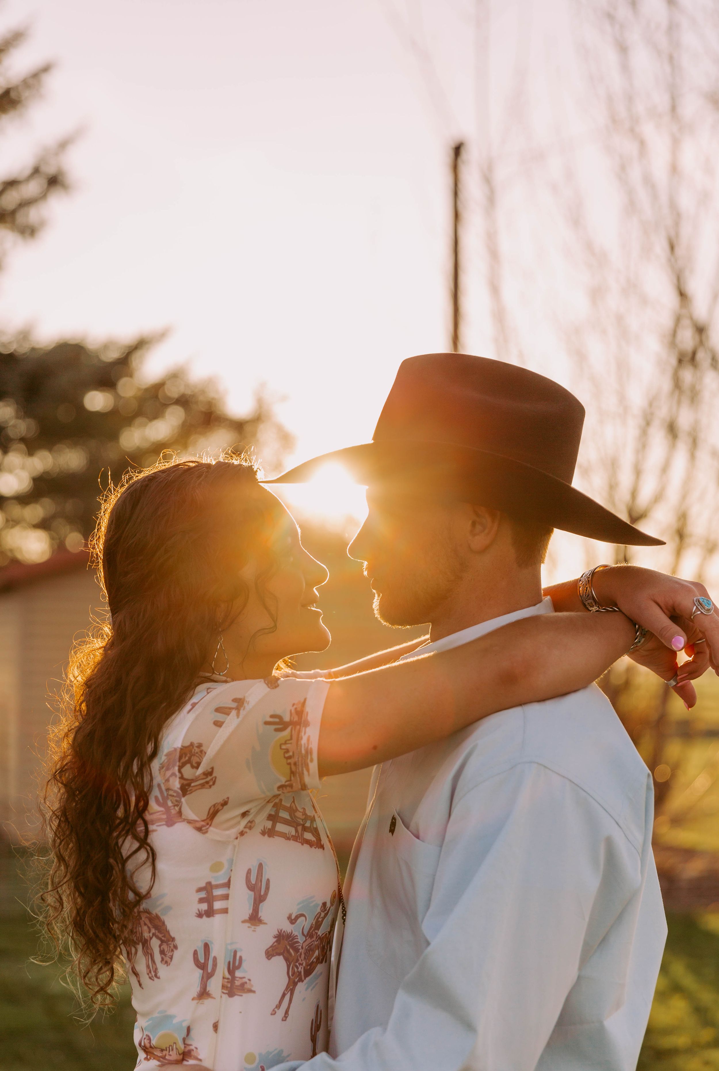A romantic couple embraces in western attire against a golden sunset backdrop.