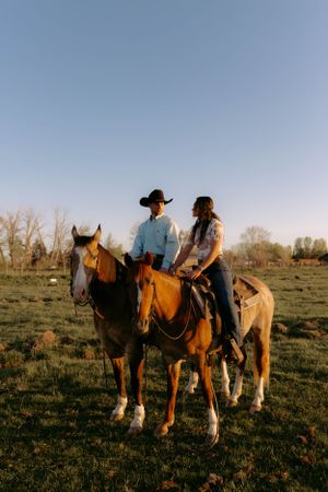 Horses and riders gather in a grassy field at sunset with mountains in the background.