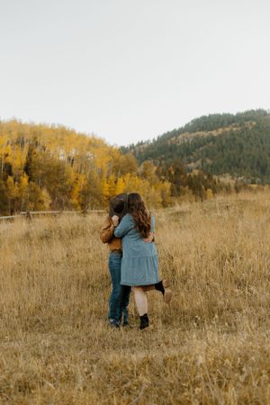 Golden autumn landscape with Western couple embracing in a meadow near mountains.