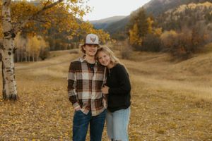 Western Couple walking through a field with fall foliage and mountains in the background.