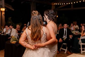 Two brides sharing a first dance embrace at an outdoor evening wedding reception.