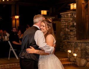 Bride in lace wedding dress sharing a tender dance with an older gentleman at wedding reception.