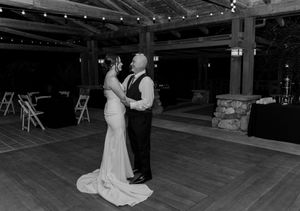 Black and white photo of bride in white gown dancing with a man at an empty wedding reception.