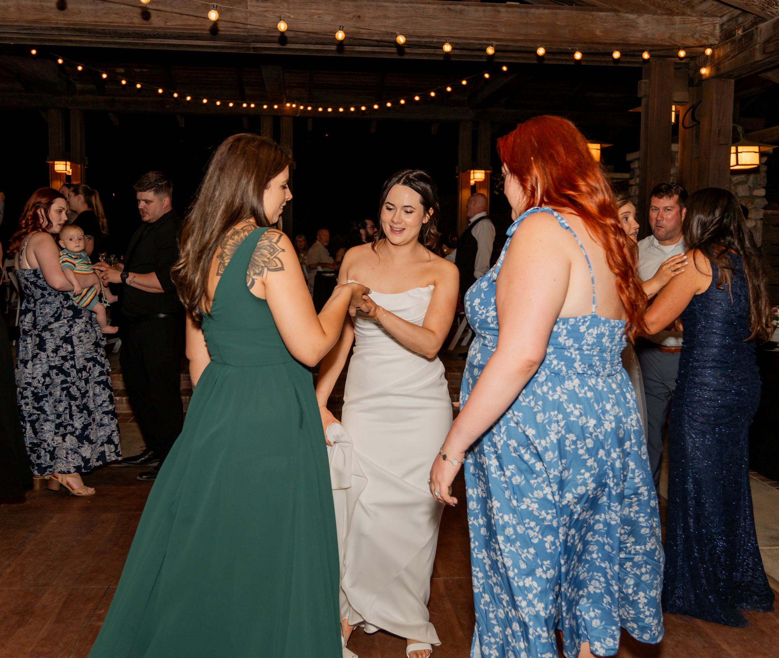 Bride in white dress dancing joyfully with guests including women in green and blue dresses.