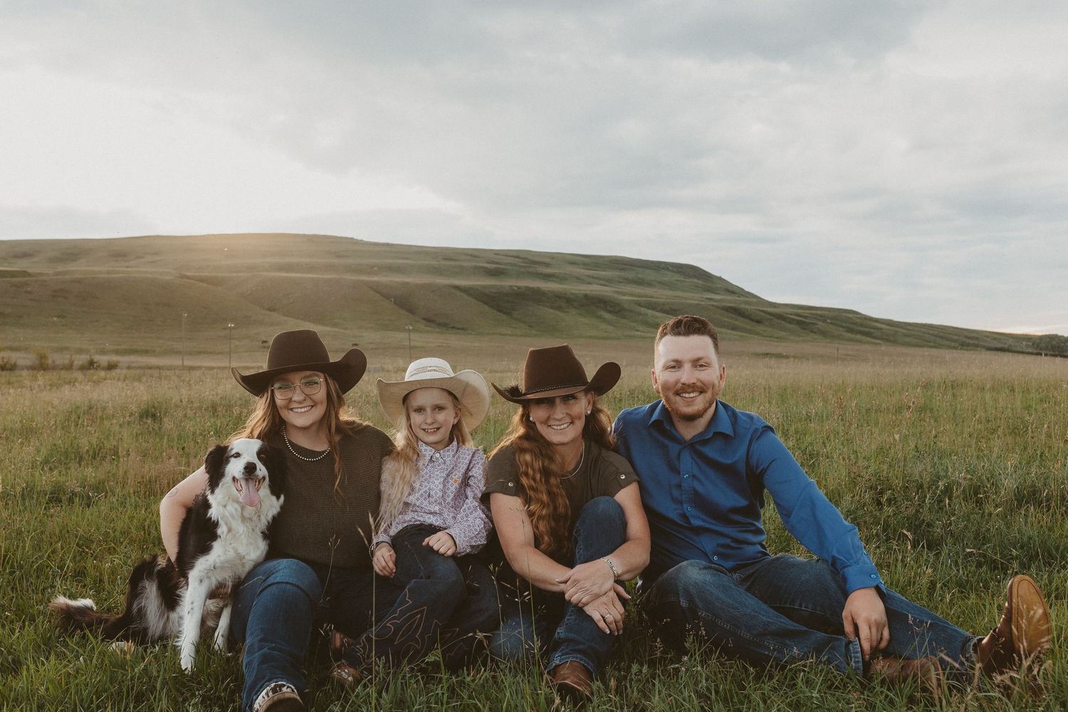 A happy family and their border collie dog pose together on a grassy hillside.