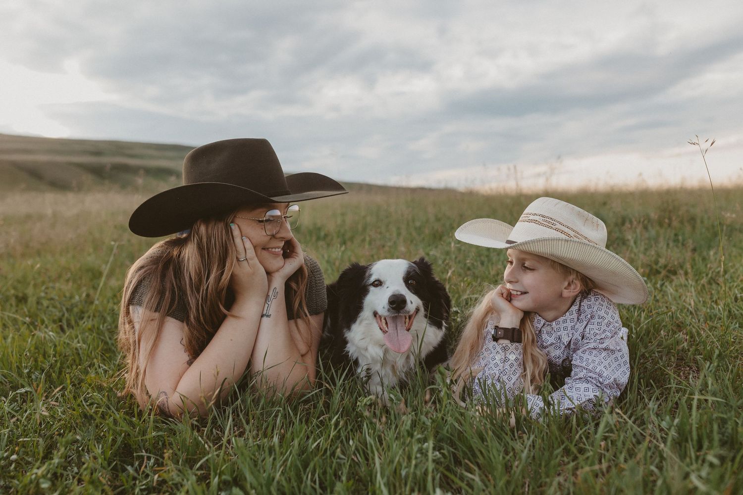 Two people and a border collie lay in tall grass during a countryside photo session.