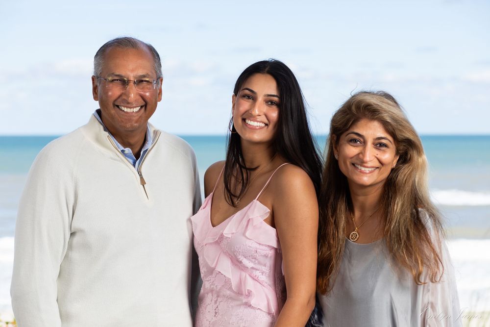 Three people standing together and smiling on a sunny beach with blue ocean in the background.