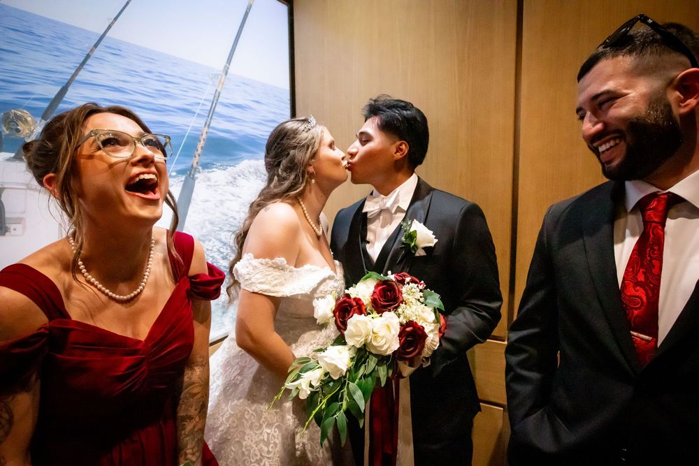 Wedding party sharing joyful laughter in an elevator with bride holding burgundy and white floral bouquet.