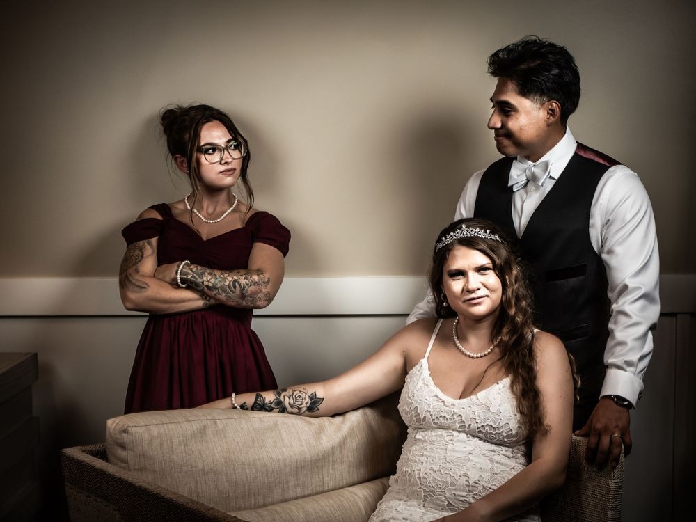 Three people in formal attire pose together during a wedding photoshoot in a moody, dramatic setting.