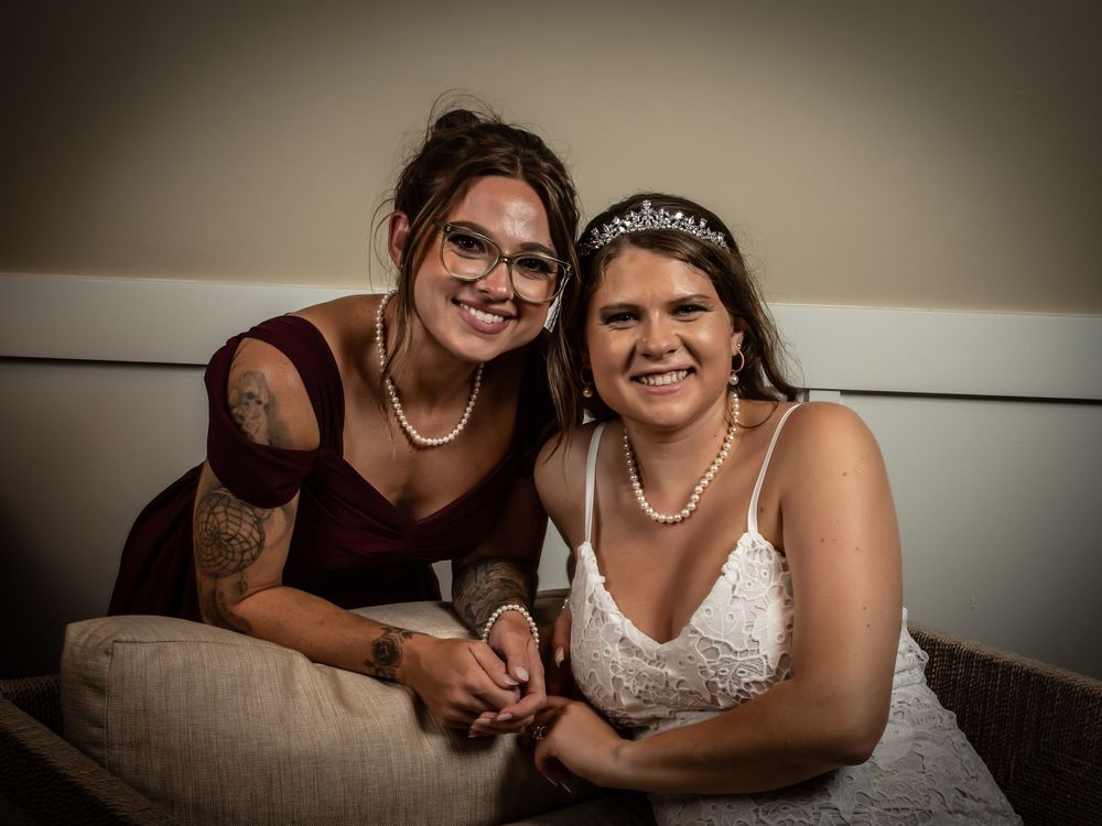 Two people wearing evening attire sit closely together on a couch, both adorned with necklaces and formal accessories.