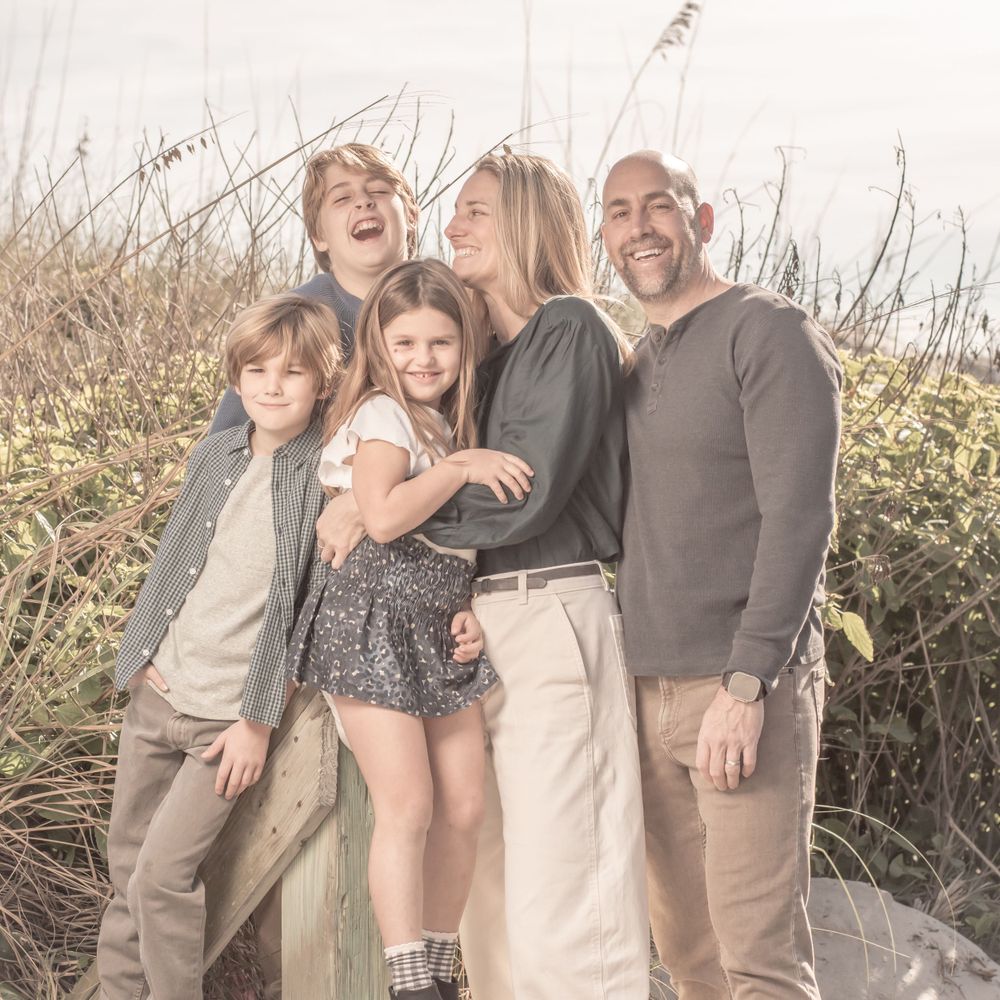 Candid family portrait of group laughing together in sunlit field of tall grass. Family portrait photography.