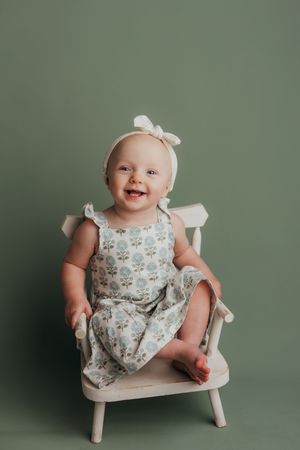 A floral dress and white bow accent this portrait against a sage green backdrop.