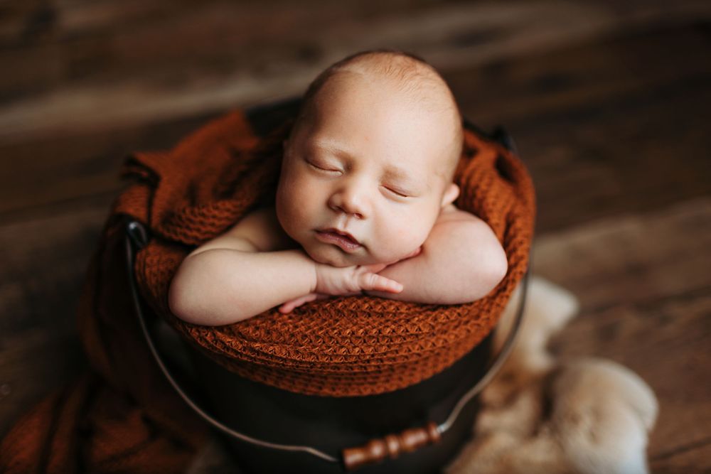 Sleeping newborn baby wrapped in brown knitted blanket rests peacefully in rustic wooden setting.