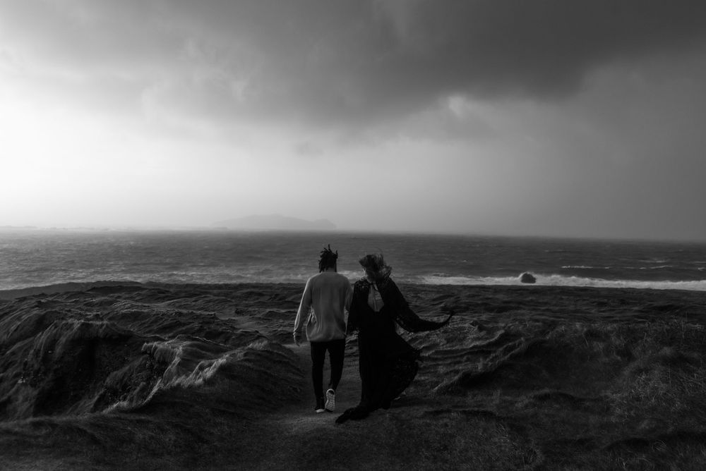 Silhouette of couple standing on dramatic coastal cliffs in moody black and white photography.