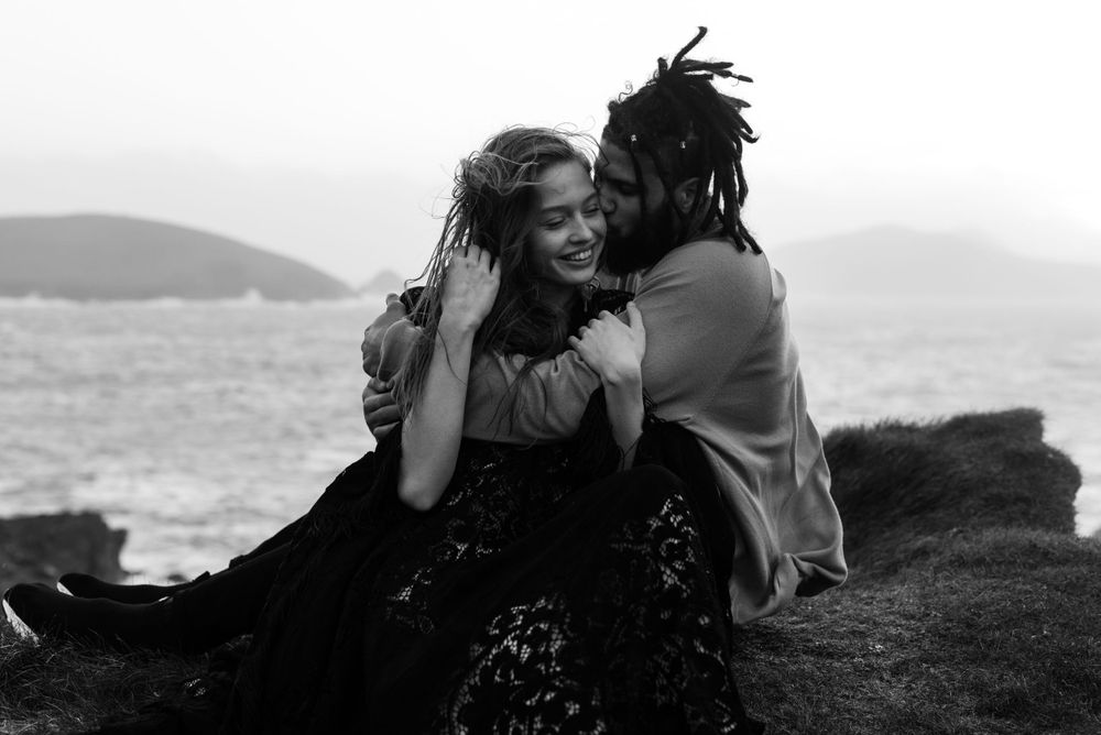 Black and white photograph of a couple laughing together on a coastal cliff.
