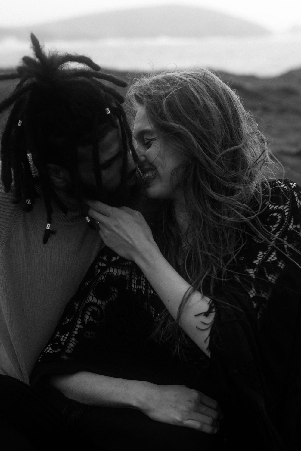 Black and white intimate portrait of two people sharing a tender moment outdoors.