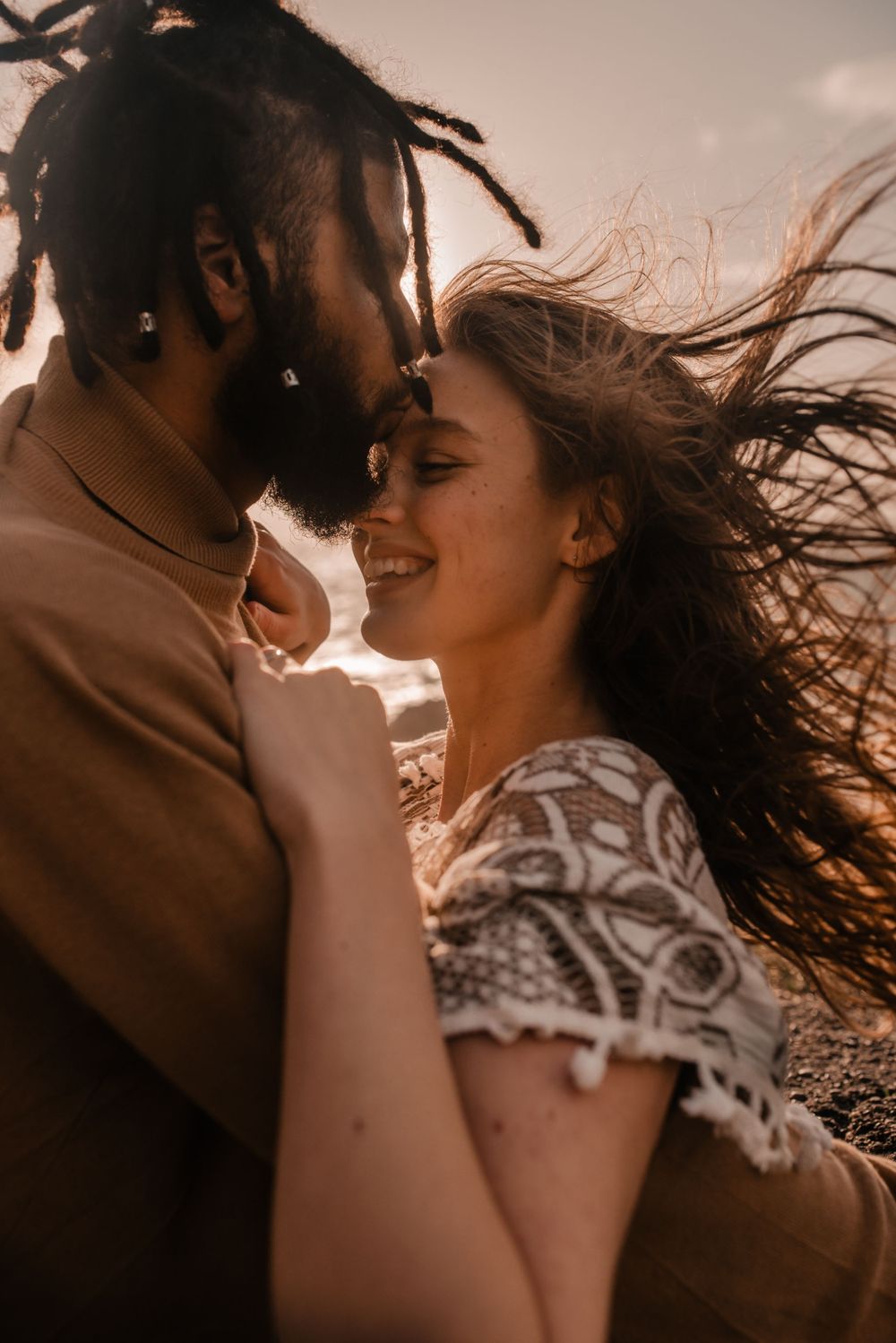 Intimate couple shares a tender moment against an ocean backdrop at golden hour.