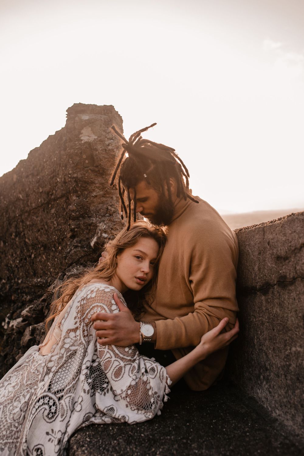Intimate couple moment captured against rocky coastal backdrop in warm evening light.
