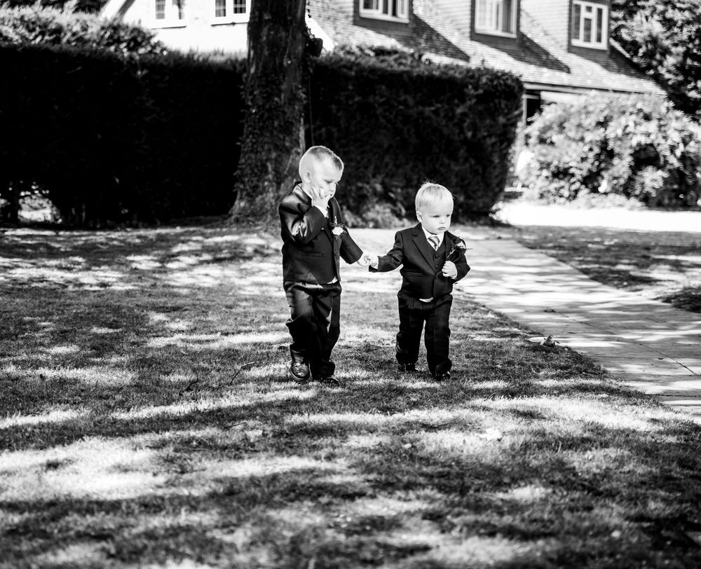 Two young boys in suits playing on grass lawn at wedding venue in black and white photo.