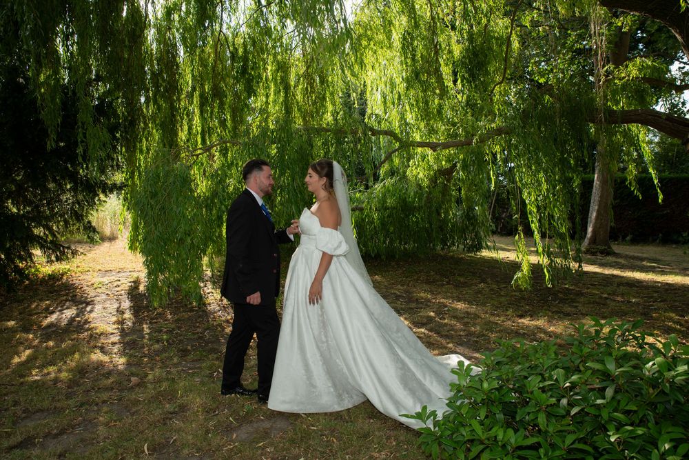 Bride and groom share a romantic moment under a weeping willow tree, bride in a flowing white gown.