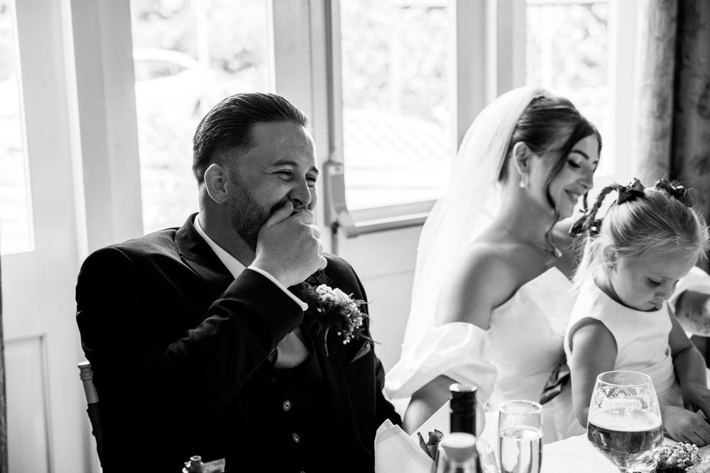 Emotional wedding guest wipes tear as bride and flower girl smile during wedding reception speech.