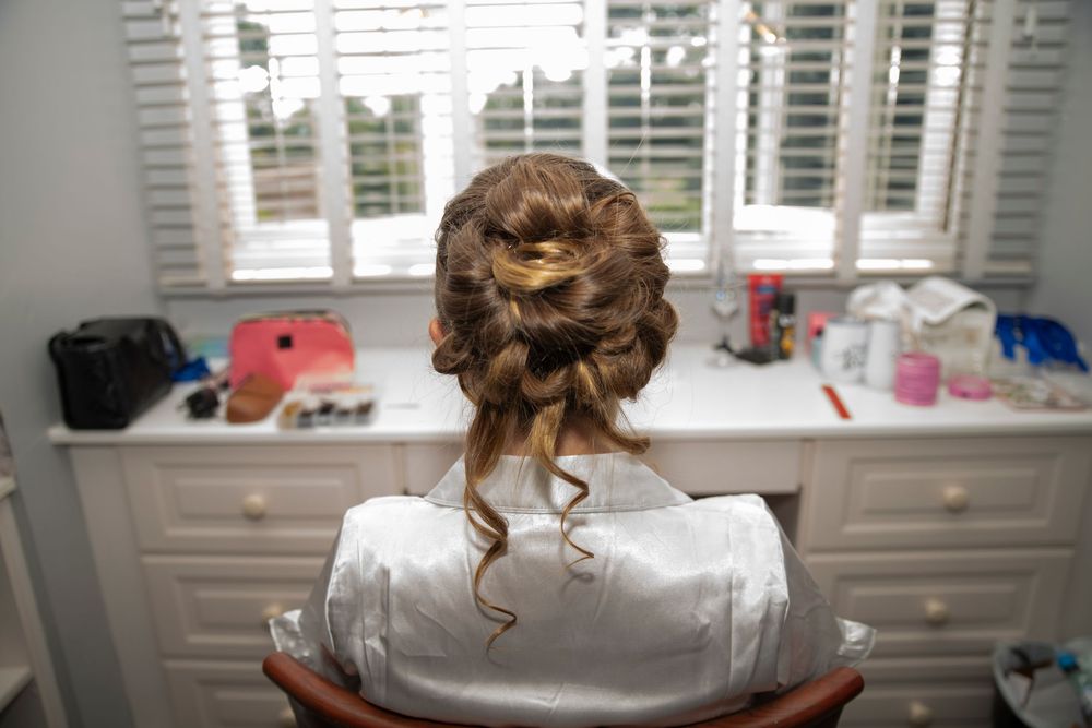 Bride with elegant updo hairstyle sitting at vanity mirror getting ready for wedding day.