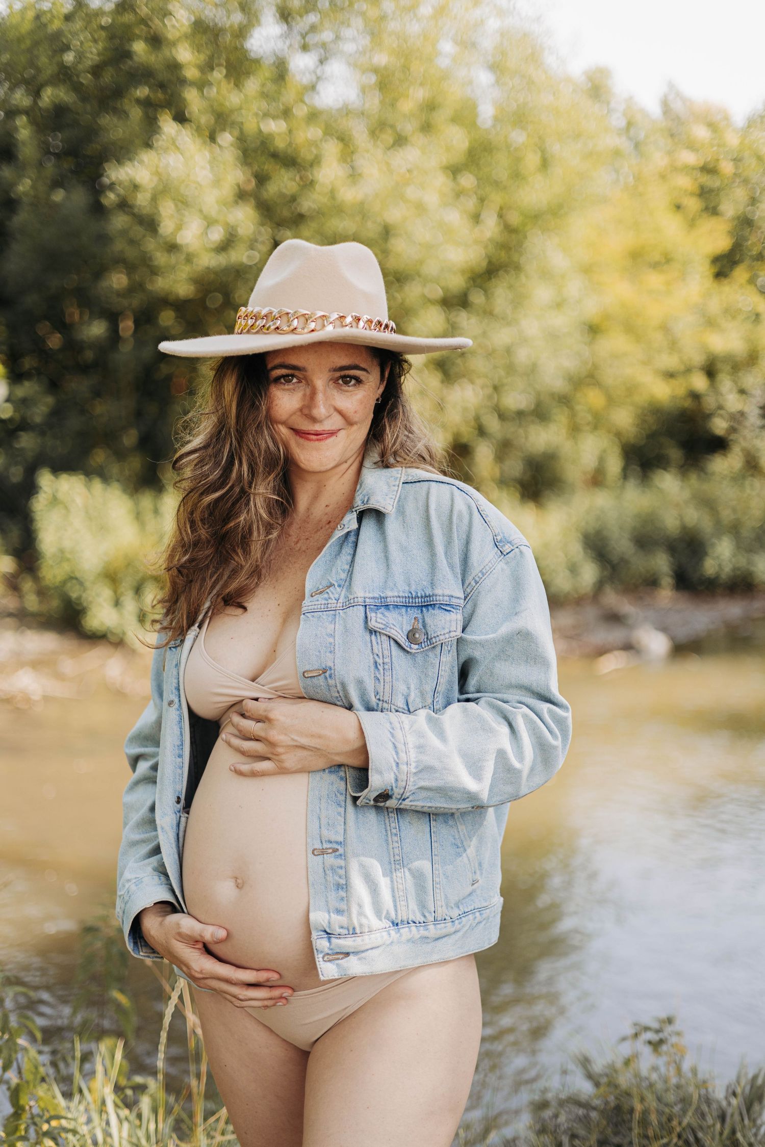 Intimate maternity photoshoot outdoors at sunset showing a couple embracing against an autumn background.