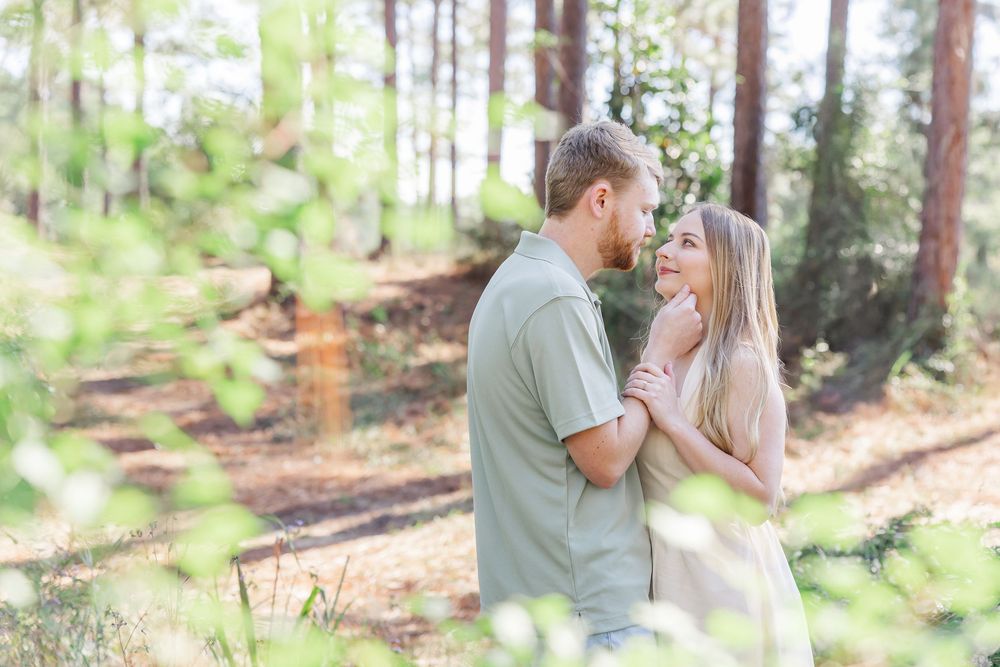 A romantic couple embraces in a sunlit forest setting during an outdoor photo session.