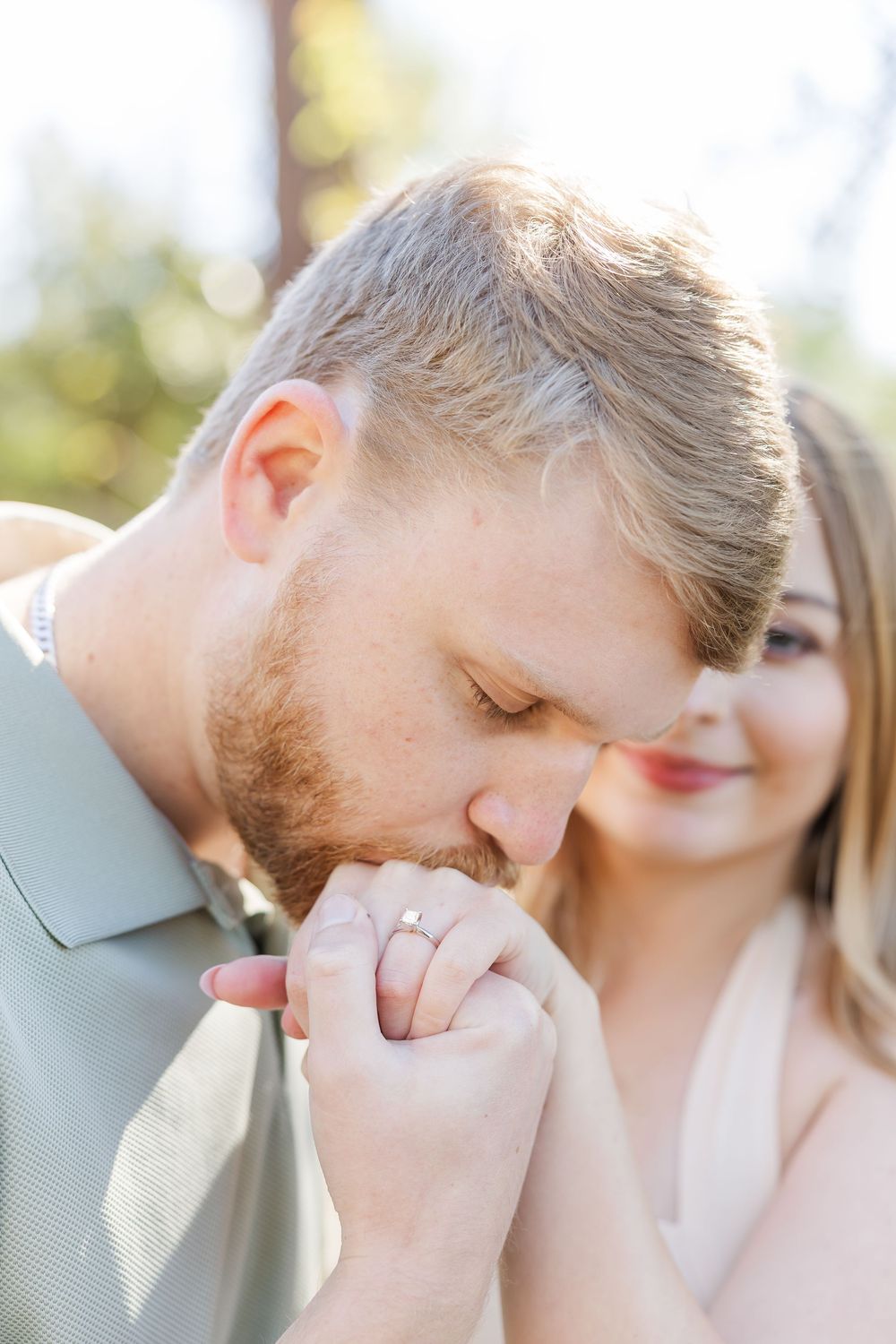 A tender romantic moment captured in soft natural lighting as a couple shares an intimate gesture outdoors.