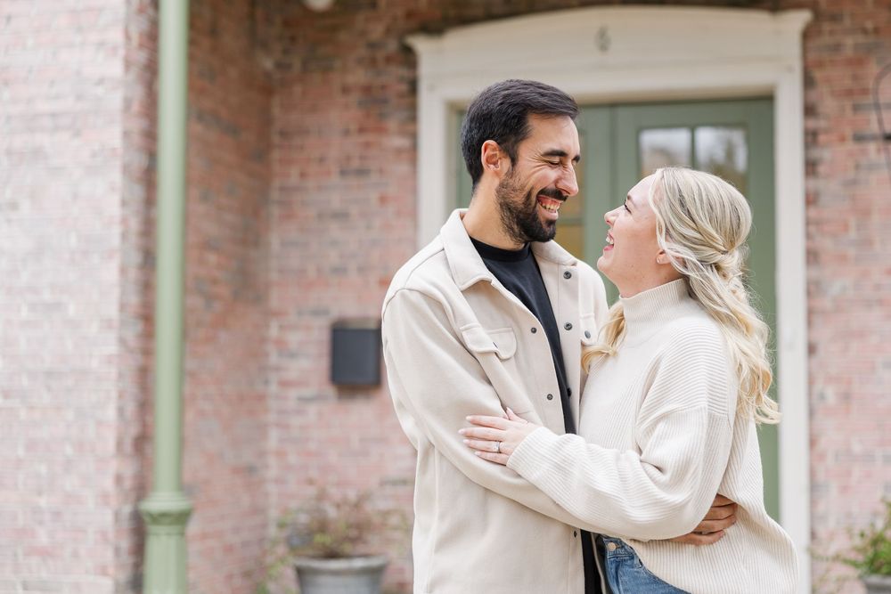 A couple in white attire shares joyful moments and embraces during an outdoor photo session at a brick building.