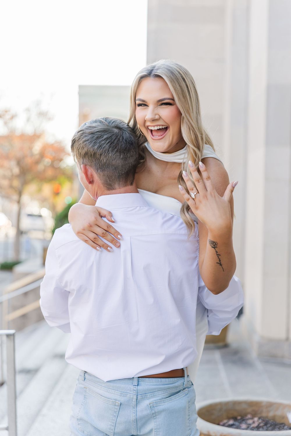 Joyful couple embracing in casual white and denim outfits during an outdoor engagement photo session.