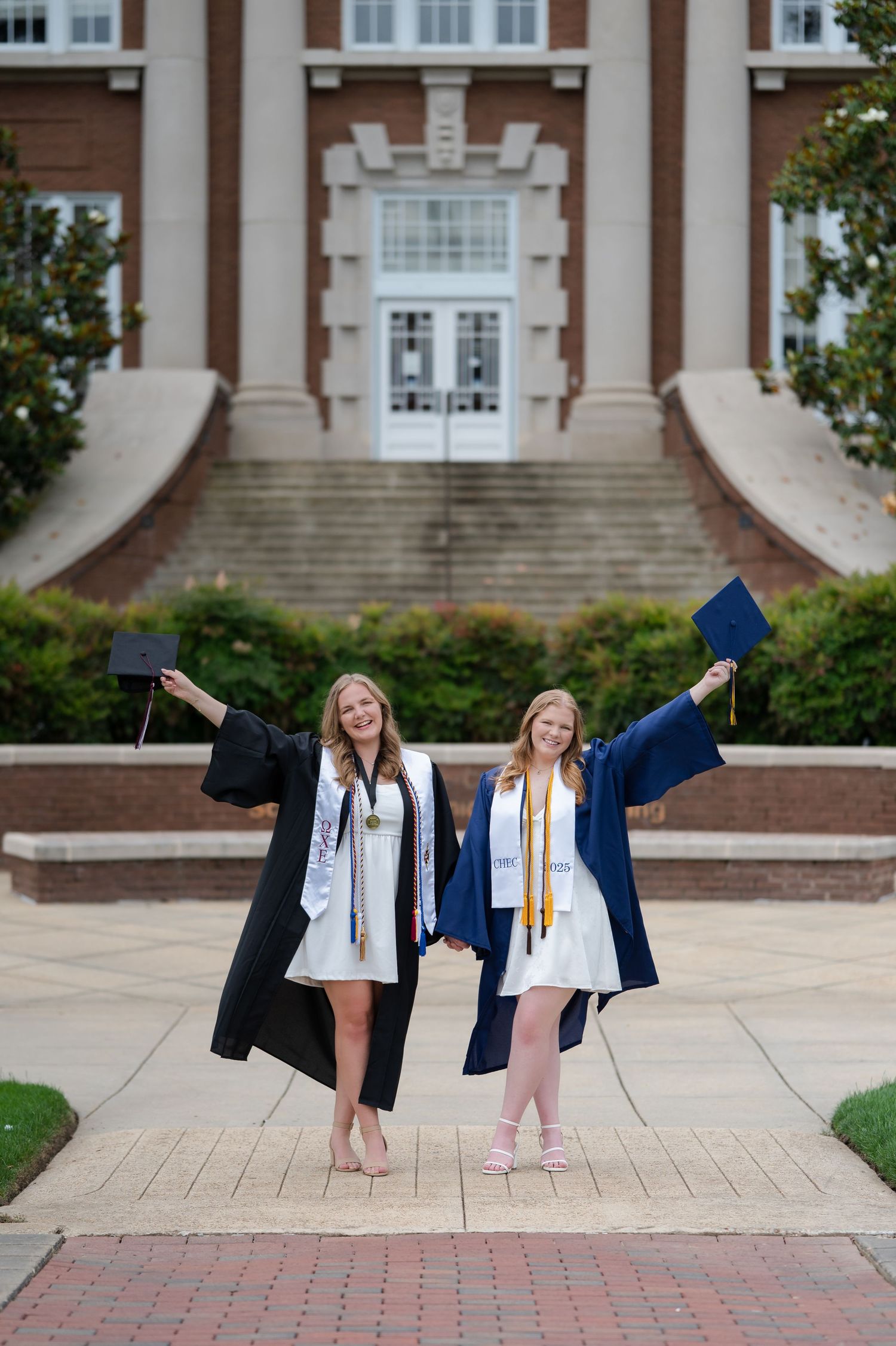 Graduate in cap and gown poses outdoors with bright smile against blurred natural background.