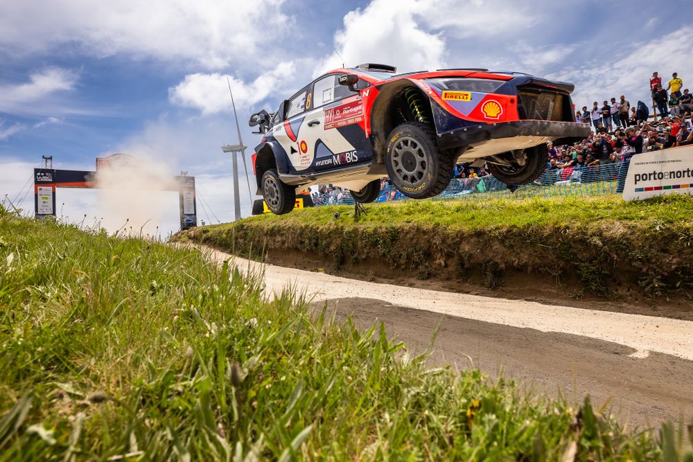 Rally car getting airborne over grass jump during competition.