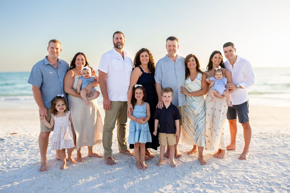 Large extended family poses together on white sand beach at sunset.