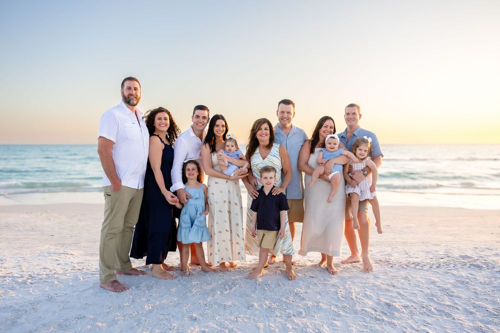 Extended family group portrait on white sand beach at colorful sunset.