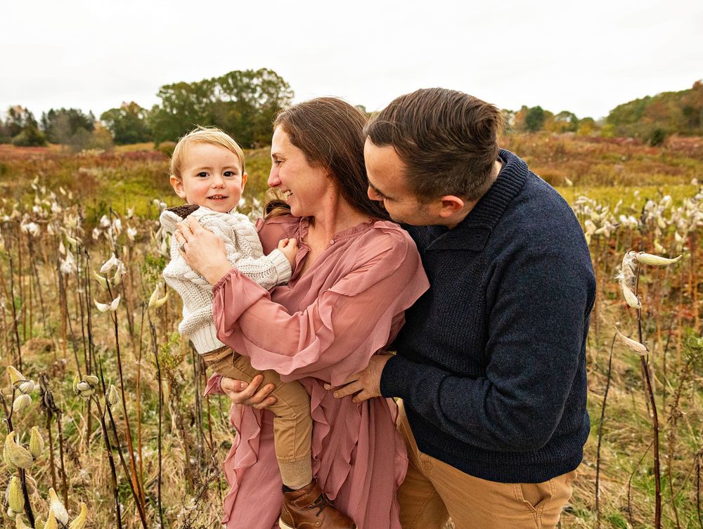 A family shares tender moments together in a golden field of dried flowers at sunset.