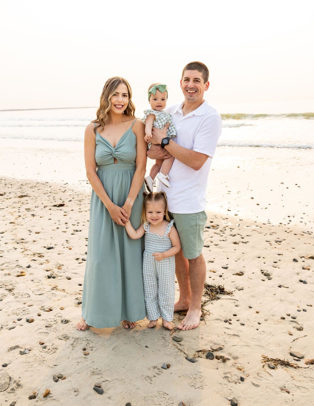 Family in coordinating outfits poses together on a sunny beach during golden hour.
