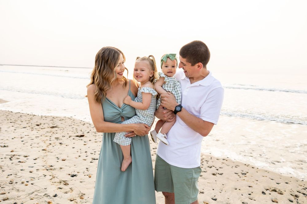 Family in coordinated blue and white outfits walking and playing together on a sandy beach at sunset.