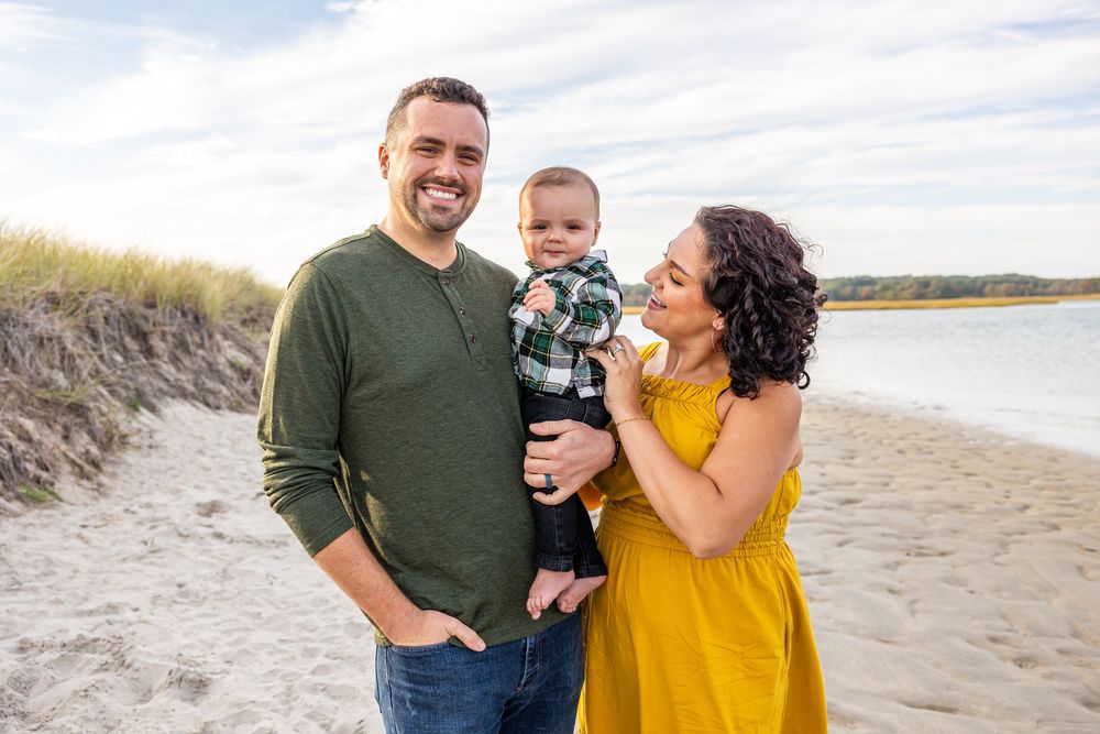A family wearing green and yellow outfits poses together on a sandy beach during a sunny day.