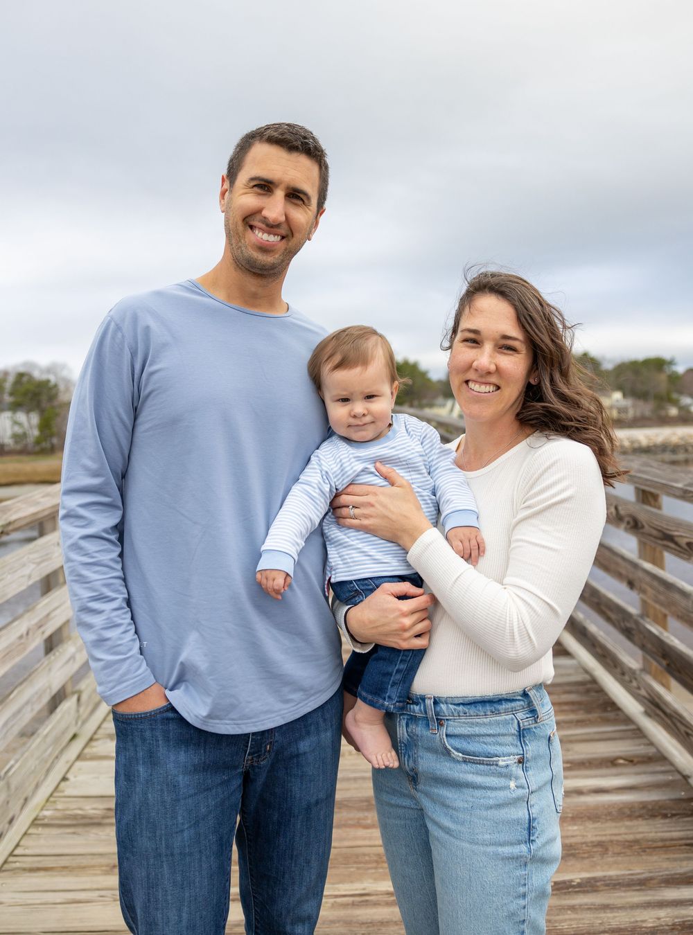 A family poses together on a wooden boardwalk with a cloudy sky backdrop on an autumn day.