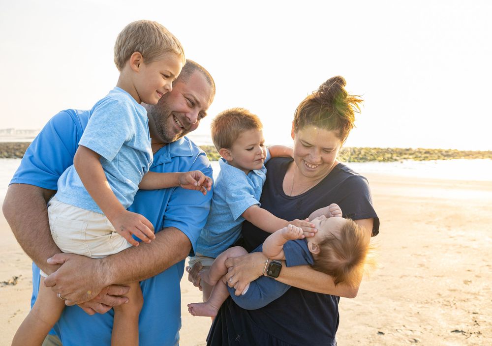 Family members wearing blue shirts embrace and laugh together on a sunny beach.
