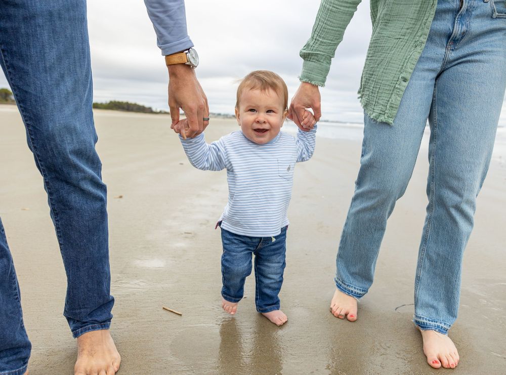 Family members walking barefoot together on wet sand at the beach during sunset.