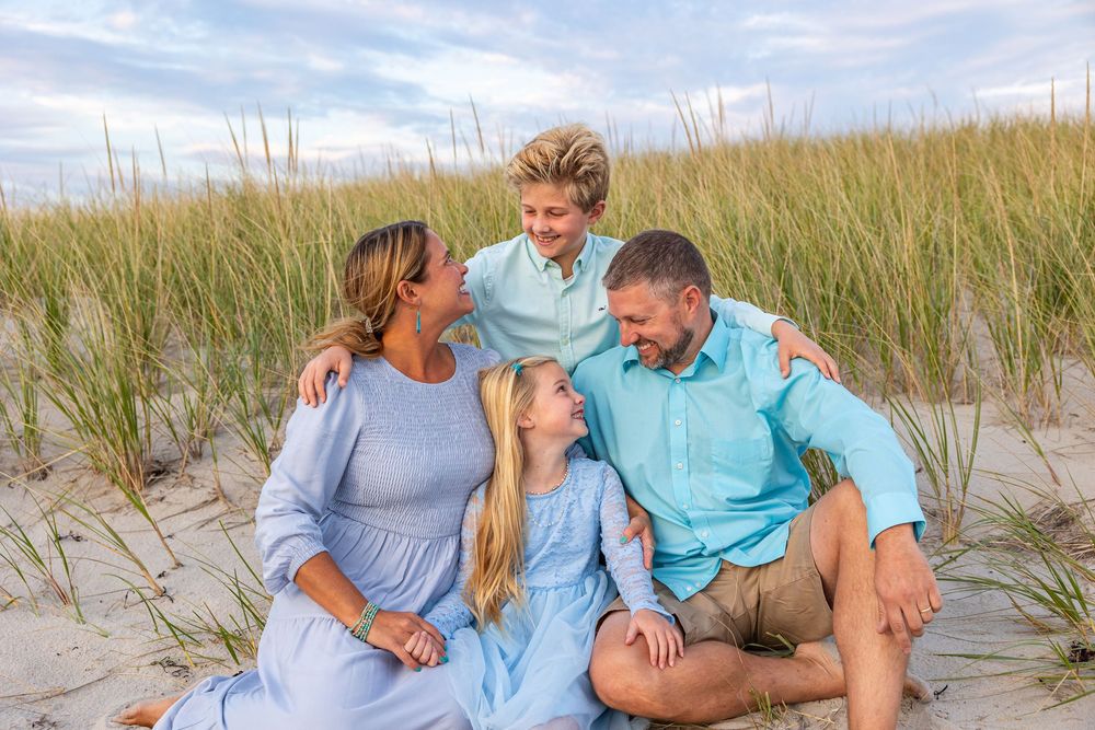 A couple shares joyful moments together on a sandy beach with sea grass and dunes in the background.