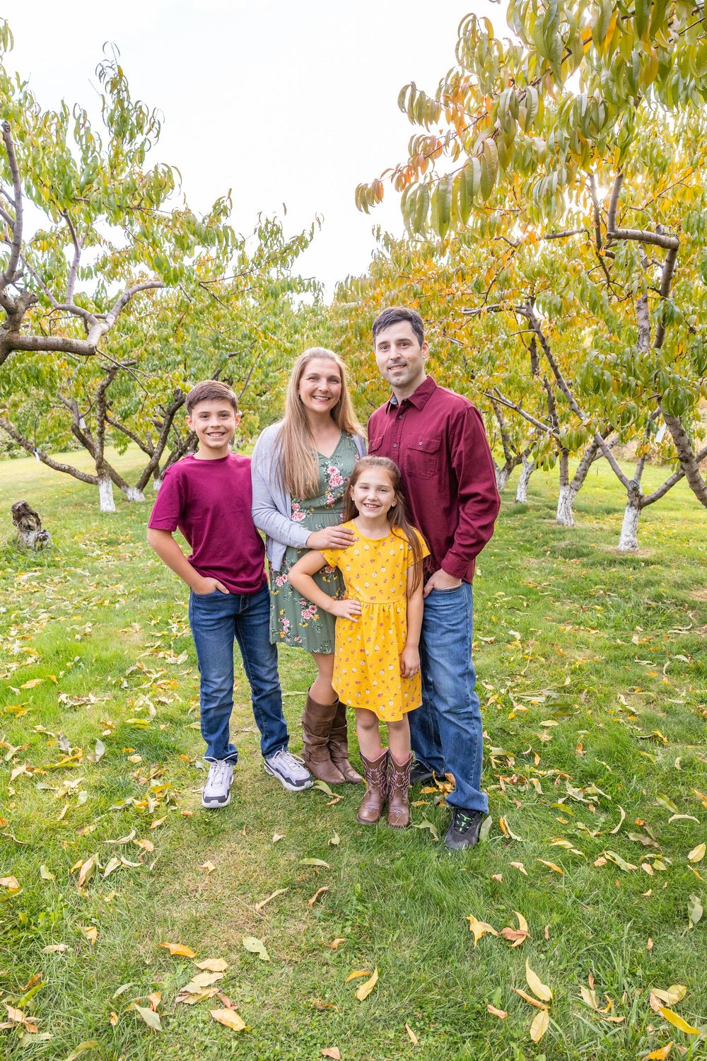 A family poses together for photos in an autumn orchard with falling yellow leaves.