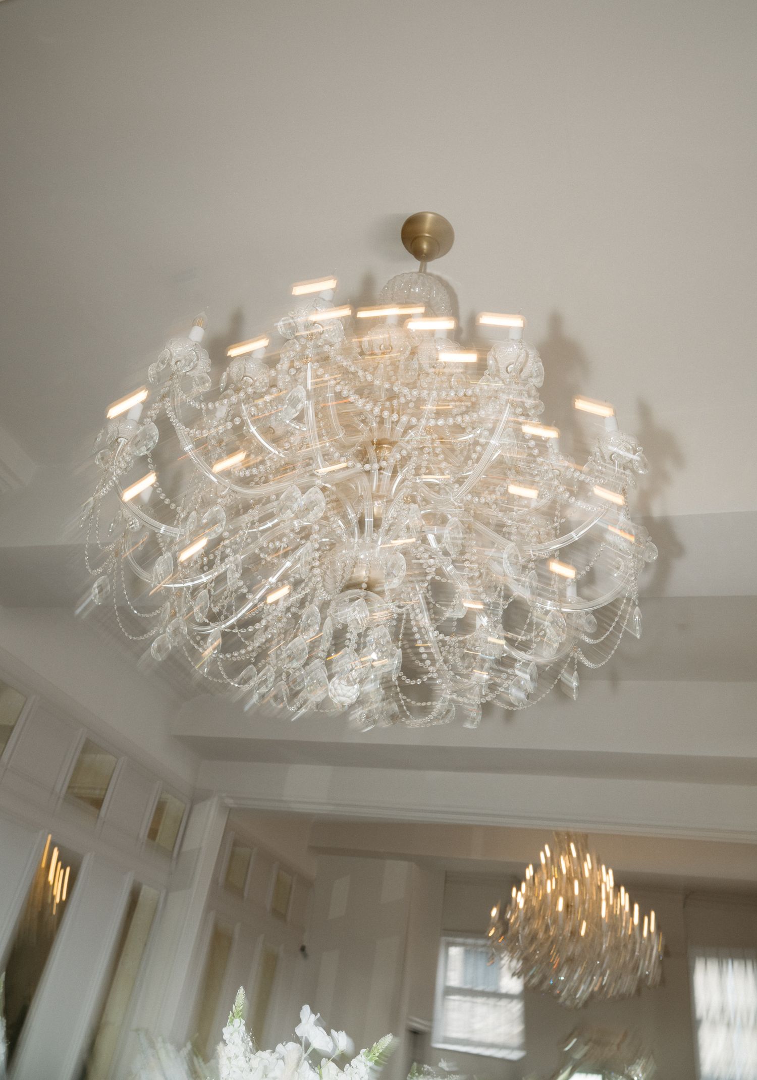 Elegant crystal chandelier with multiple tiers of delicate glass pieces illuminates a white ceiling in a luxurious room.