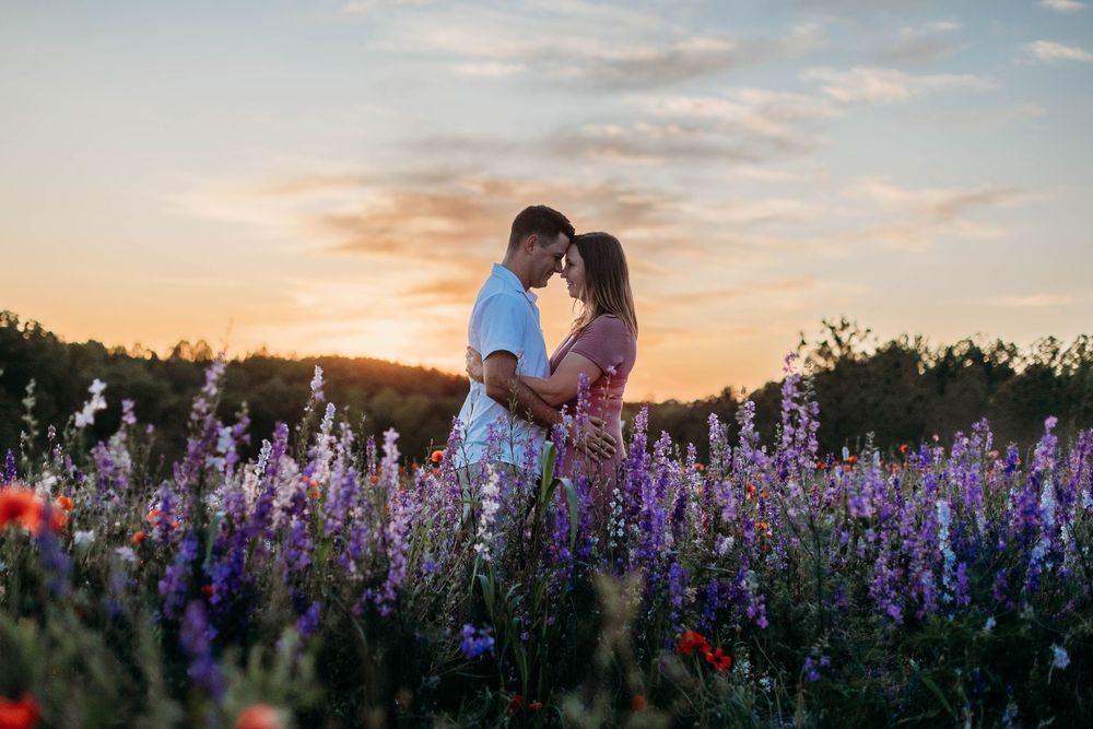 Couple embracing in a vibrant wildflower field at sunset, surrounded by purple lavender and red poppies.