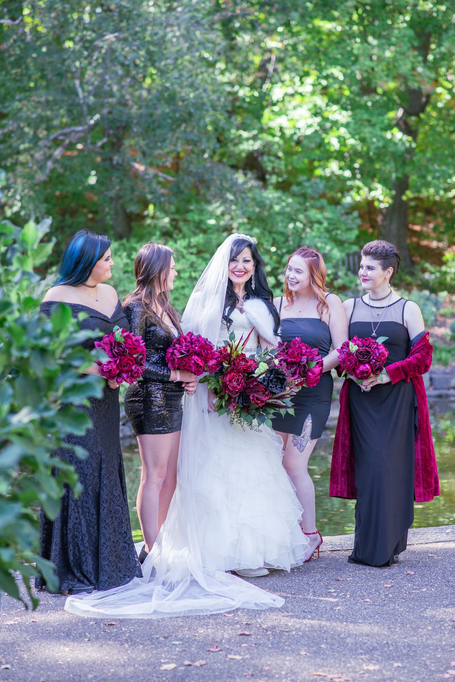 Bride with her four bridesmaids holding their red and black flowers smiling at each other.
