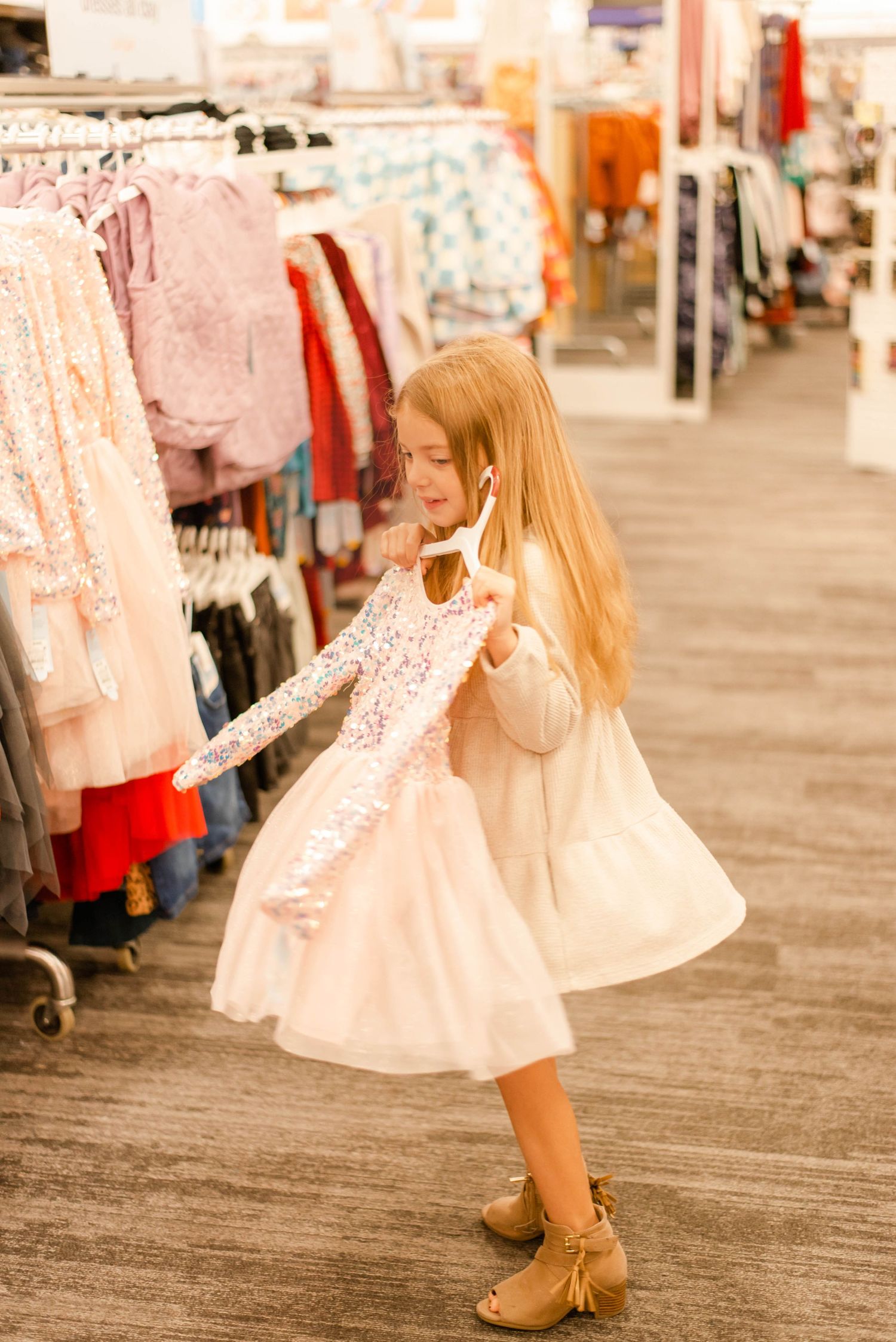 Girl in white dress twirling while shopping in clothing department.