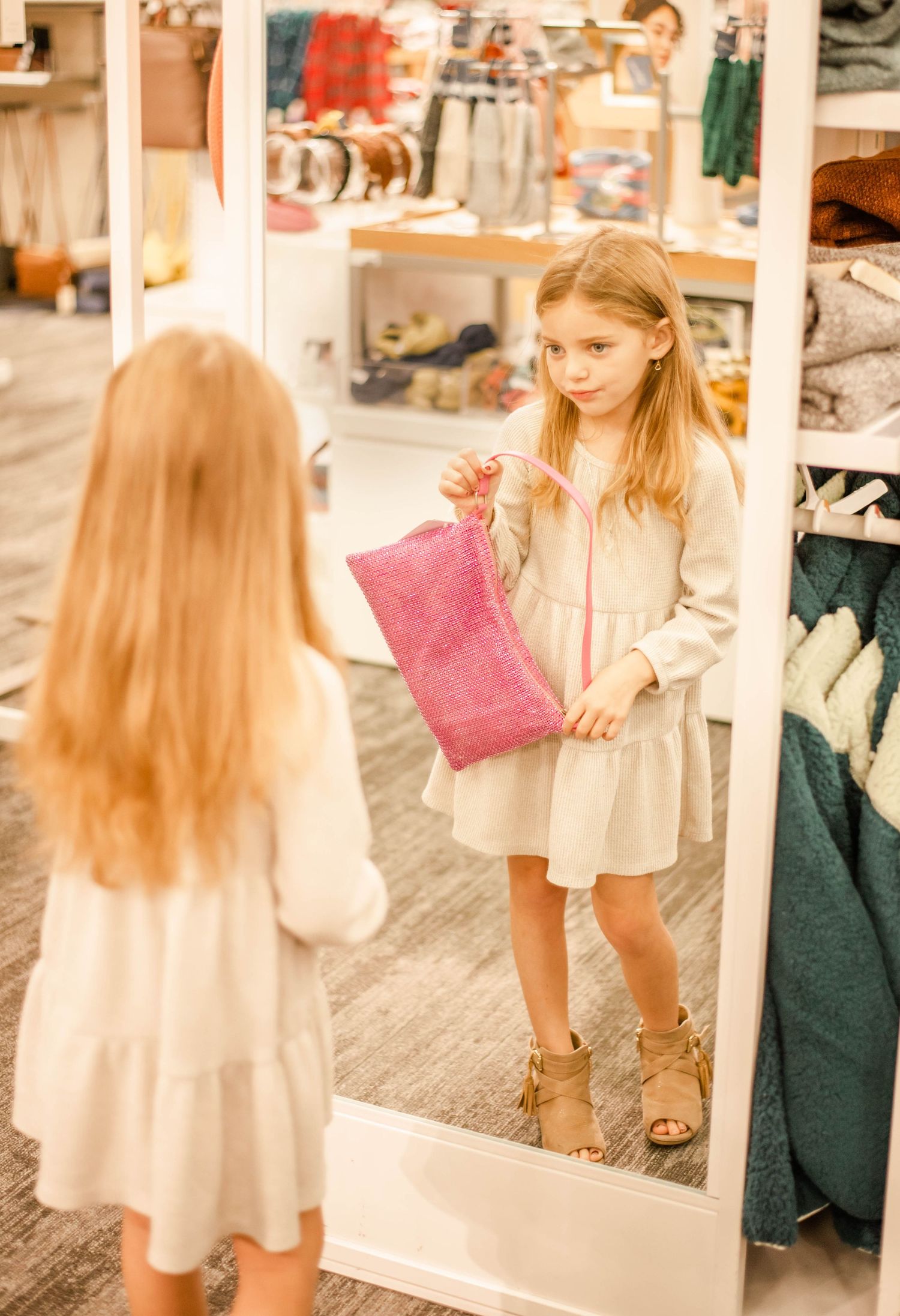 Girl in white dress looking at pink accessory while checking mirror in store.