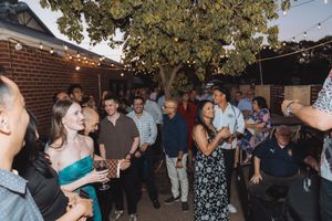 People gathered outdoors for a social event under trees with string lights creating a festive atmosphere.